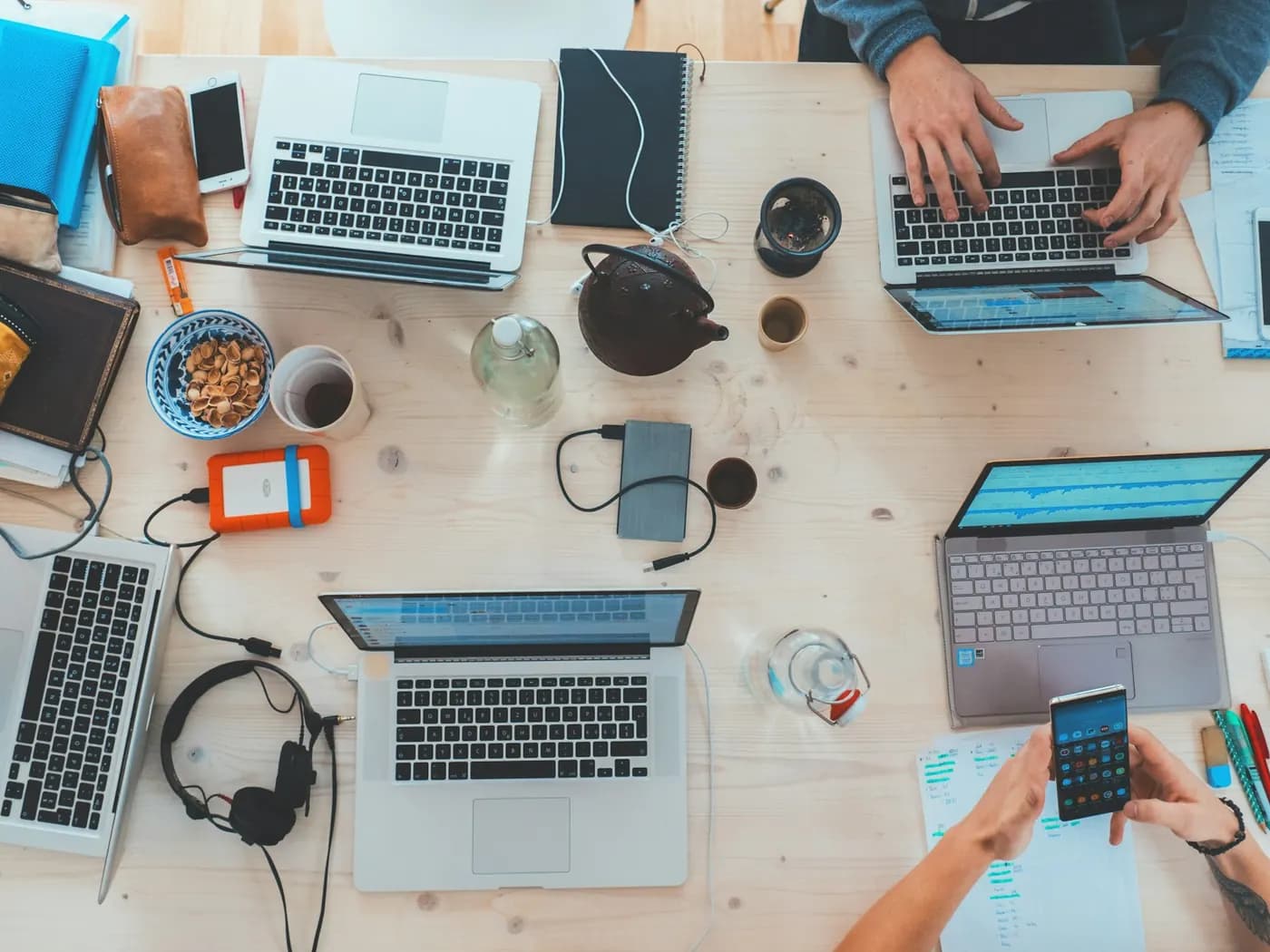 Laptops, keyboards, headsets and mobile devices laid out on a shared workbench